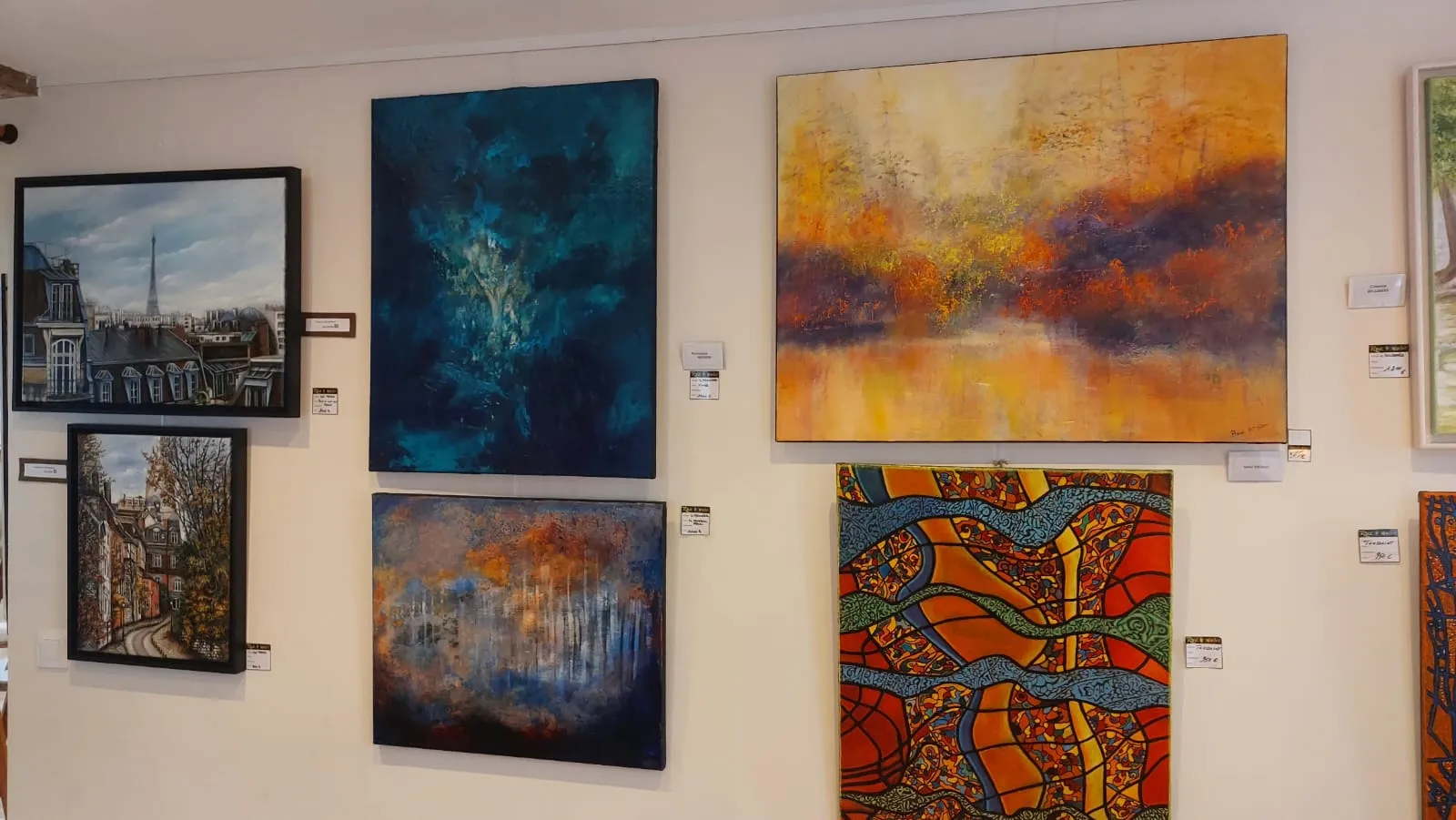 Mur d'accrochage de la galerie : peintures de Paris encadrées et grands formats abstraits, cartels visibles