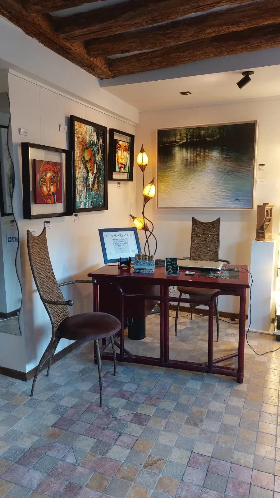 Bureau d'accueil de la galerie sous les poutres anciennes, portraits encadrés et grande toile de sous‑bois