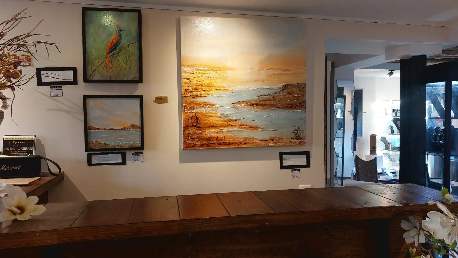 Comptoir en bois de la galerie, marine dorée au mur et vitrine de bijoux en arrière‑plan